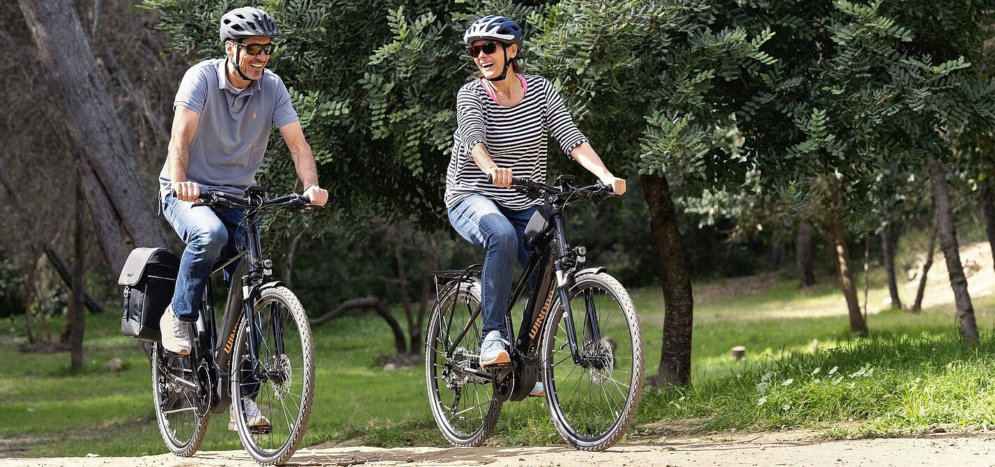 E-Dossier Cover Eine Frau und ein Mann fahren auf Elektrofahrrädern durch den Wald.